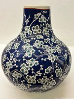 Front view of blue ceramic vase decorated with raised white and green prunus blossoms, showing overall design and shape.
