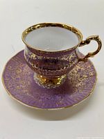 Front angle view of the purple tea cup with gold floral detailing and matching saucer beneath