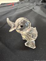 Clear crystal duck figurine on black background, showing faceted body, detailed wings and open beak.