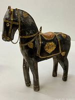 Full view of the wooden horse figurine showing the dark wooden surface and gold-toned decorative metal harness and plaques.