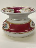 Side view of white porcelain spittoon featuring burgundy band with floral decorations and gold trim.
