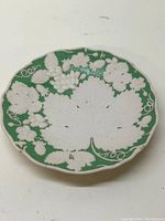 Top view of the antique plate showing white vine leaves and grape motifs embossed on green background