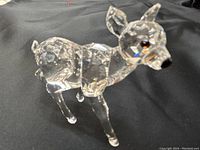 Photo showing front diagonal view of Swarovski crystal fawn figurine on black fabric. Clear crystal with brown eyes and black nose visible.