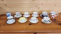 Full display of nine tea cups with matching saucers and one blue and white mug arranged on wooden table