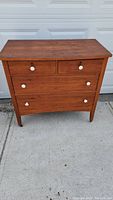 Full front view of antique wooden dresser with four drawers and white knobs placed on concrete background.