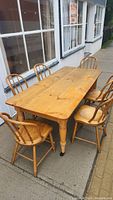 Full view of pine harvest table with six matching spindle-back chairs arranged outdoors