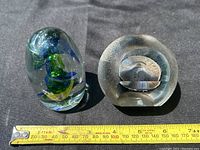Two art glass paperweights shown side by side with measuring tape for size reference on black cloth background.