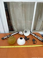Photo shows entire lot laid out including two adjustable desk lamps, two lamp shades (one yellow textured glass, one white metal), and lamp parts including plugs and socket.