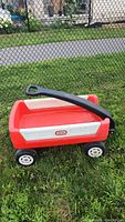 Photo of red and white Little Tikes wagon with black handle on grass, side view showing overall condition.