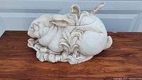 Full view of white ceramic rabbit-shaped tureen on wooden surface showing the whole piece and intricate leaf details.