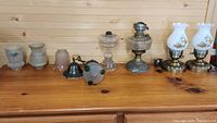 Photo showing nine items on wooden surface including various glass lamp shades, oil lamps, and glass parts.
