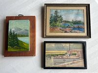 Three watercolour paintings arranged on a white surface: one on wood board, two framed.