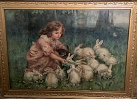 Front full view of framed chromolithograph featuring a young girl in a pink dress feeding a group of white rabbits outdoors in green grass and flowers.