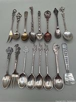Full set of 16 souvenir spoons and one fork arranged in two rows showing varying figural tops and handles.
