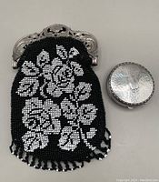 Photo showing black and white floral beaded purse with silver frame next to round silver compact