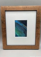 Full view of the framed painting showing the gold textured wooden frame and white mat surrounding the abstract artwork.