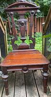 Front view of an antique Eastlake style walnut hall chair showcasing the carved back with finials and the front legs.