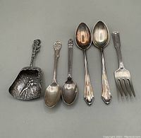 Six piece lot showing two spoons with ornate handles, two smaller coffee spoons, a heavily embossed Dutch sugar shovel, and a baby fork with patterned handle.