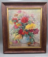 Full view of the original floral still life painting on board with frame, showing a vibrant bouquet with red, yellow, pink, and other colored flowers in a blue vase on a neutral background.