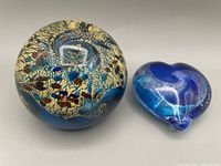 Two Robert Held paperweights, round and heart-shaped, against a neutral background.