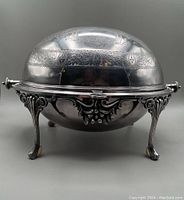 Front view of silver plated roll top serving dish closed, showing domed lid with etched decorative patterns and ornate legs.