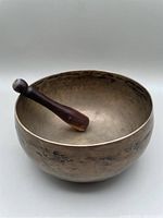 Brass singing bowl with wooden mallet resting inside bowl, showing size and condition