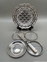 Photo of lot showing sterling butter dish with glass liner, butter spreader with mother of pearl handle, two small monogrammed sterling dishes, and three glass coasters with sterling rims.