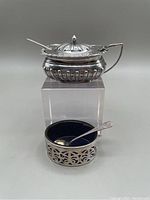 Photo showing the covered salt cellar with hinged lid and gold washed salt spoon, alongside the open salt cellar with cobalt liner and sterling spoon.