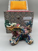 Front view of the Taiwanese ceramic dragon figurine in front of its decorative fabric-covered box with an orange cushion inside.