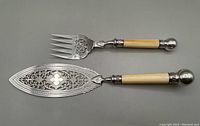 Fish serving fork and knife with ornate pierced silver blades and natural handles, showing overall good antique condition