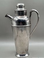 Front view of the vintage hammered cocktail shaker with lid on top, clear view of the handle and spout.
