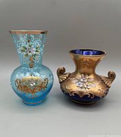 Front view of two vintage Bohemian glass vases with hand painted flower decorations and gilding, shown side by side.