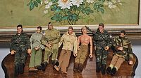Seven plastic military action figures, seated, showing variation in uniform style and pose.