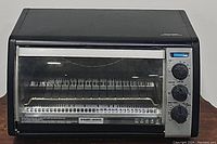 Front view of the Black & Decker Black CTO6120B toaster oven showing clear glass door, wire rack inside, and three control knobs on the right.
