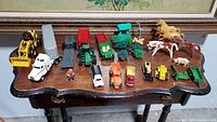 Photo of various farm toys on wooden table including vehicles, animal figurines, trees, and a farmer figure.