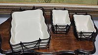 Photo of 2 smaller rectangular white ceramic loaf pans with raised white floral pattern in black metal wire baskets with handles on wooden table.