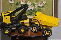 Photo showing Tonka Mighty Crane and Buddy L Big Bruiser dump truck side by side on a wooden table with floral background.