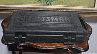 Closed black plastic Craftsman branded carrying case with front latches and handle, placed on a wooden table.