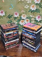 Two stacks of DVD movies on wooden table with floral wallpaper in background.