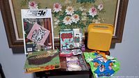 Photo of all lot items displayed on a table, showing latch hook kit, puzzle box, stationery sets, balloon kit, stickers bag, pencil case, McDonald's bag, and keychain.