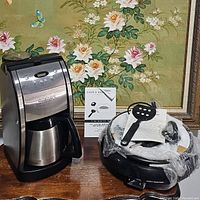 Photo showing the Cuisinart grind and brew thermal coffeemaker and the cooks essential electric deep skillet with spatula and instruction manuals on a wooden surface.