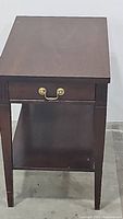 Front view of vintage mahogany end table showing drawer and shelf.