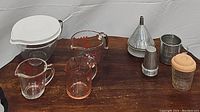 All items in the set displayed together on wooden surface and white backdrop. Items grouped with measuring cups front and center, funnels, tin cups placed to the right.