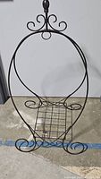 Front view of the large tear drop-shaped metal plant stand showing the decorative curved metal frame and grid platform for placing plants.