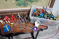 Overview of multiple plastic action figures including Power Rangers, medieval warriors, and Transformers placed on and next to a wooden table