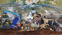 Three labeled resealable plastic bags containing mini plastic toys: one with mixed mini cars and plastic people, one with animal figures including dinosaurs, and one with plastic wrestler figurines