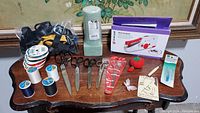 Full view of sewing tools and supplies on a wooden table including scissors, threads, ribbons, foam inserts, pin cushion and Singer Stitch Sew Quick boxed tool.