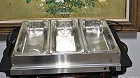 Front view of the electric buffet server and warmer showing three stainless steel compartments with lids, indicator light, and temperature control knob.