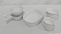 Full view of the entire Corning Ware bakeware batch showing two saucepans with lids, one large oval baking dish and four round baking dishes.