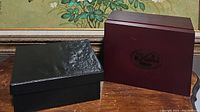 Two collectible boxes for La Vigna wine and champagne accessory sets; one maroon with logo, one black textured.